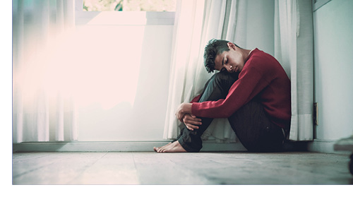 Man sitting in corner of room with head on knees