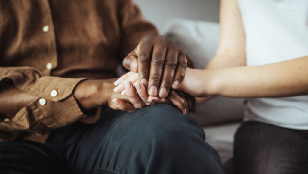 Two people sitting holding hands in comforting fashion